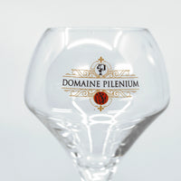 Verre à vin transparent avec logo Domaine Pilenium doré et rouge sur fond blanc